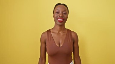 Işıl ışıl parlayan Afro-Amerikan kadın, kollarını kavuşturmuş, mutlu gülümsemesini sergiliyor. çarpıcı bir izole edilmiş sarı arkaplana karşı başarının ifadesi.