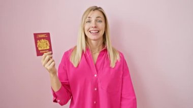 Neşeli genç sarışın kadın, muzaffer bir zaferle kollarını kaldırmış, Kuzey İrlanda pasaportunu pembe izole edilmiş arka planda tutan kirişler. Başarılı başarının kutlaması.
