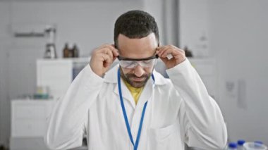 Laboratuvar önlüklü, kendine güvenen bir İspanyol modern bir laboratuvarda güvenlik gözlüklerini ayarlıyor..