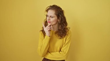 Güzel genç bir kadın, kafa karıştırıcı bir şüpheyi merak ederek dalgın dalgın duruyor. Çenesinde bir parmak, yukarı bakıyor, sarı bir arkaplanda izole bir şekilde..
