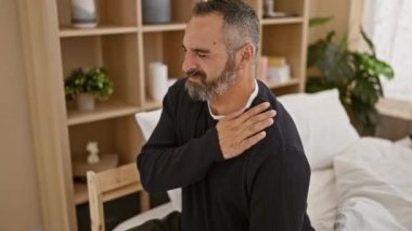 Yaşlı, sakallı, kır saçlı, acı içinde yüzünü buruşturan, rahat bir yatak odasında omzuna dokunan bir adam.