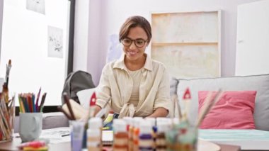 Zafer kazanan, genç, çekici İspanyol kadın sanatçı neşeli zaferi sevinçle kutluyor kanepede gülümseyerek ve samimi stüdyoda kazanan bir ifadeyle.