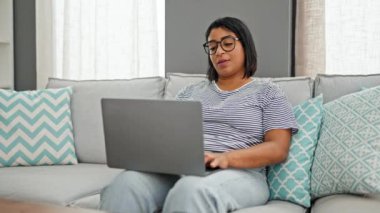 İspanyol kadın oturma odasında dizüstü bilgisayarı kapatıyor, kanepede televizyon seyretmeye hazırlanıyor, evde rahat ediyor..