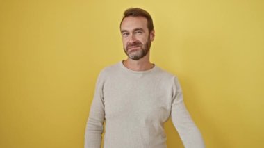 Neşeli orta yaşlı İspanyol adam, kendine güvenerek ayakta duruyor ve bir numaralı parmağını işaret ediyor, gülümsüyor, güneşli, sarı izole bir duvara karşı, cazibeyle dolup taşıyor..