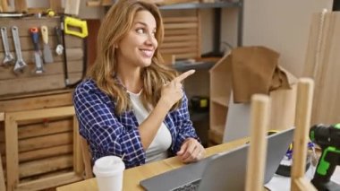 Neşeli genç Latin kadın sevinçle ışıldıyor, bir elinde parmaklarıyla, marangozluk atölyesindeki bir masada rahatça otururken. Onun doğal, mutlu ifadesi bulaşıcıdır.!