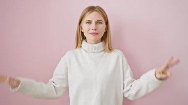 Çekici sarışın kız sevinçle işaret ediyor, parmaklarıyla neşeli bir yedi gösteriyor. Canlı, pembe, izole bir arka plan karşısında durmak, mutluluk yayıyor..