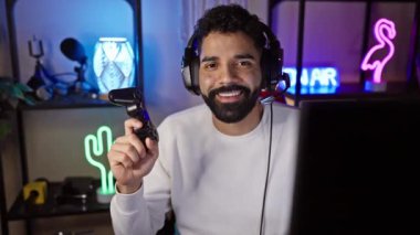 Geceleri neon ışıklı bir odada kulaklıklı, gülümseyen sakallı bir adam oyun oynuyor.