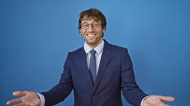 Arkadaşça bir gülümseme ile mutlu genç bir adam, sıcak bir hoş geldin jesti ile kollarını açık, güzel izole mavi bir arka plan karşı poz