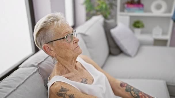 Yaşlı Gri Saçlı Rahatlamaya Sarılmış Bir Kadın Oturma Odasındaki Kanepede — Stok video