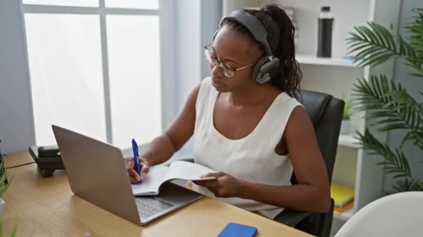 Фокусована Афроамериканка Навушниками Використовуючи Ноутбук Роблячи Нотатки Сучасному Офісному Інтер — стокове відео