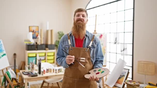 自信を持って若い赤毛の男のアーティストの絵筆を手に 屋内アートスタジオで喜んで微笑みます — ストック動画