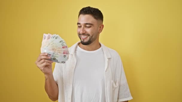 エキサイティングな若いアラブ人男性 誇らしげに育てられた腕の中で銀行券を保持し 勝利と成功を祝い 黄色の孤立した背景で幸せなビーム — ストック動画