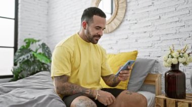 Modern yatak odasında akıllı telefon kullanan sakallı yakışıklı bir İspanyol.