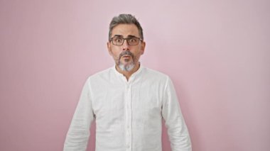 İzole edilmiş pembe arka planda sürpriz bir ifadeyle duran Latin kökenli gri saçlı genç adam.