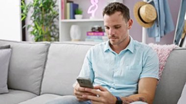 Sakallı, gevşemiş bir İspanyol adam modern oturma odasında akıllı telefon kullanmaktan zevk alıyor. Bu da evde rahatlık ve rahatlık anlamına geliyor..