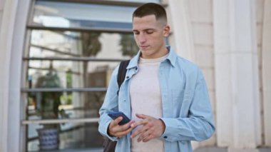 Camdan yapılmış şehir binasına karşı akıllı telefon kullanan sıradan giyinmiş genç bir adam..