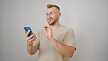 Sakallı yakışıklı bir genç, beyaz bir arka planda akıllı telefonuyla video izlerken gülümsüyor..