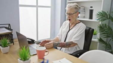 Gülümseyen kıdemli gri saçlı kadın çalışan, ofisteki başarısını kutluyor. Akıllı telefonunu kazanan bir hareketle kullanıyor.