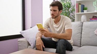 Modern bir apartman dairesinde akıllı telefon kullanan yakışıklı bir İspanyol..