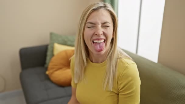 若い金髪の女性は 面白い表現で幸せな舌を突き刺すTシャツを着ています 感情コンセプト 自宅で — ストック動画