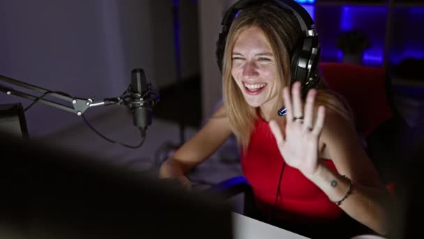一个快乐的金发女人 带着耳机 晚上在灯光昏暗的游戏室里与智能手机互动 — 图库视频影像