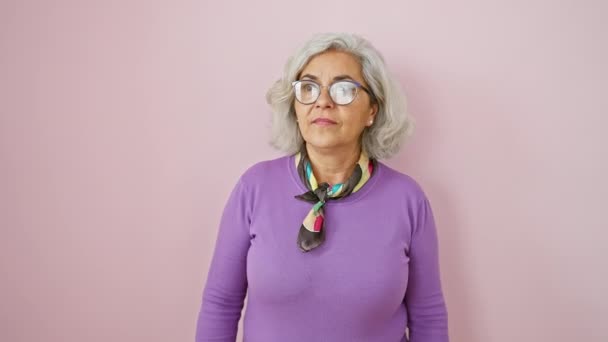 中年女性が眼鏡をかけ 先を指差した ピンクの背景に隔離された何かに対する驚くべき表現で灰色の毛髪とオープンマウス — ストック動画