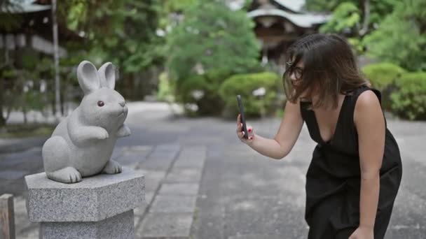 Cheerful Hispanic Woman Dons Glasses Capturing Beautiful Picture Rabbit Statue — Stock Video