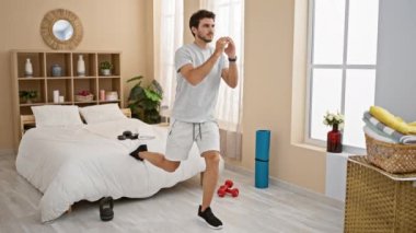 Parlak bir yatak odasında spor aletleri ve yoga minderiyle egzersiz yapan yakışıklı bir adam evde sağlıklı bir yaşam tarzını simgeliyor..