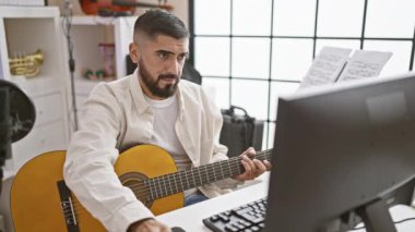 Müzik stüdyosunda gitar çalan sakallı yakışıklı bir adam.