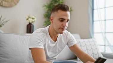 Rahat bir genç adam akıllı telefon kullanıyor ve sıcak bir kanepede kahve içiyor..