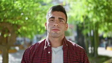 Kendine güvenen, kenar mahalle parkında mutlu bir şekilde duran, mutlu bir şekilde gülümseyen çekici, yakışıklı, neşeli yetişkin, doğanın tadını çıkaran, kendinden emin bir adam.