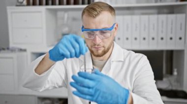 Odaklanmış sakallı bir adam, koruyucu giysiler giyerken modern bir laboratuvar ortamında deneyler yapıyor..