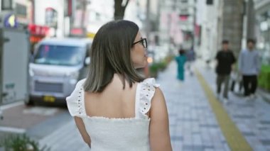 Güzel bir İspanyol kadının Tokyo caddesinde yürüdüğünü, gözlükleriyle kentsel çevreye baktığını, şehrin hayatını ve mimari güzelliğini yakaladığını.