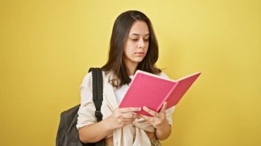 Genç ve güzel bir İspanyol kadının neşeli portresi, güneşli sarı bir arka planda izole bir şekilde okul kitabını okurken kendinden emin bir şekilde bir jest yapıyor.