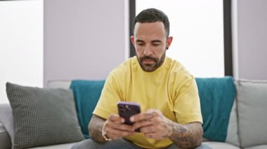 Modern bir oturma odasında akıllı telefon kullanan odaklanmış sakallı bir adam..