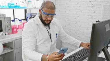 Laboratuvar önlüklü adam modern laboratuvar ortamında akıllı telefon kullanıyor..