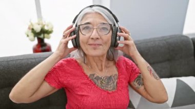Kendine güveni tam orta yaşlı bir kadın kulaklıklarını çıkartıyor, evdeki kanepesinde müzik dinledikten sonra rahatlıyor.