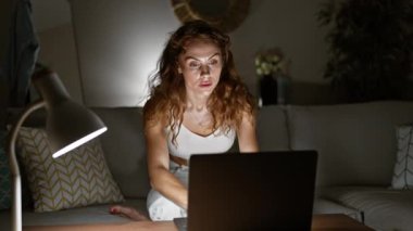 Evde dizüstü bilgisayarda çalışan beyaz bir kadın, gece lambayla aydınlatılmış, odaklanmayı ve kendini adamayı çağrıştırıyor..