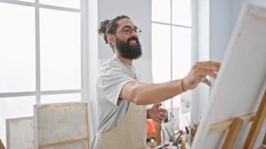 Parlak bir sanat stüdyosunda resim yapan mutlu sakallı adam yaratıcılığını ve gündelik tarzını sergiliyor..