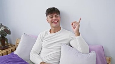 Kendinden emin ve neşeli, genç İspanyol adam yatak odasındaki pijamalarıyla uzanır. Mutlu bir şekilde ofsayt bir yeri işaret ediyor. Yüzünde dostça bir gülümseme parlıyor..