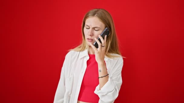 一个金发碧眼的女人在一个充满活力的红色背景下 用智能手机交谈时的情绪反应 — 图库视频影像