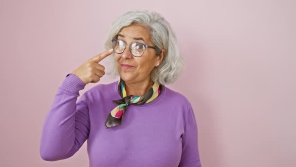 輝く灰色の髪型 眼鏡着用 中年の女性はうまく彼女の鼻を指差し ピンクの背景に微笑んで — ストック動画