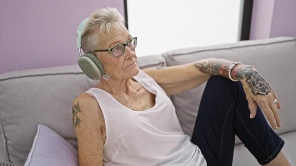 シニア白髪の女性リスニング音楽に座ってソファに家 — ストック動画