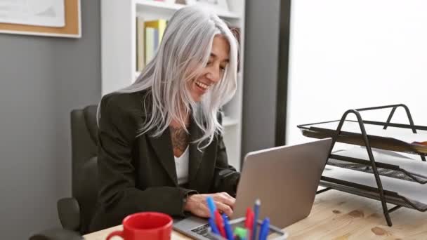 オフィスでラップトップで働く 歯ぎしりした 自信を持った中年の女性 魅力的な笑顔でポジティブな姿勢と幸せを表現する灰色の髪型 — ストック動画