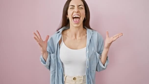 勝利とカジュアルな服装のビームで楽しい若いヒスパニック女性 孤立したピンクの背景に輝かしい笑顔と勝者の表現で彼女の勝利を祝う — ストック動画