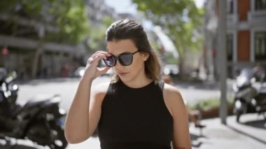 Işıl ışıl genç İspanyol kadın hareketli Madrid sokaklarında güneş gözlüğü takarken ciddi bir ifade takınıyor.