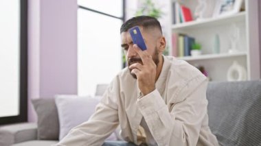 Evde kredi kartı tutan sakallı dalgın bir adam.