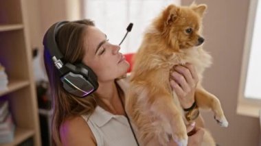 Gülümseyen İspanyol asıllı genç bir kadın oyun için sevgisini paylaşıyor, karanlık bir odada, kendinden emin ve yanında köpek varken, oyun kulaklığı kullanarak.