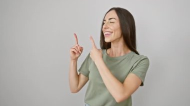 Neşeli, gündelik giysiler içinde genç bir İspanyol kadın kameraya güvenilir bir gülümseme göstererek izole edilmiş beyaz bir duvarda boş bir alanı işaret ederek sizi sunuyor ve hoş geldiniz diyor..