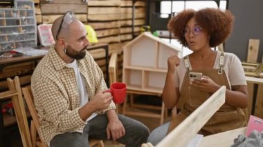 İki çalışkan marangoz, erkek ve kadın, hareketli marangoz stüdyolarında kahvenin tadını çıkarıyorlar, akıllı telefonlarına dalmışlar, marangozluk işiyle ilgili derin bir sohbet içindeler..